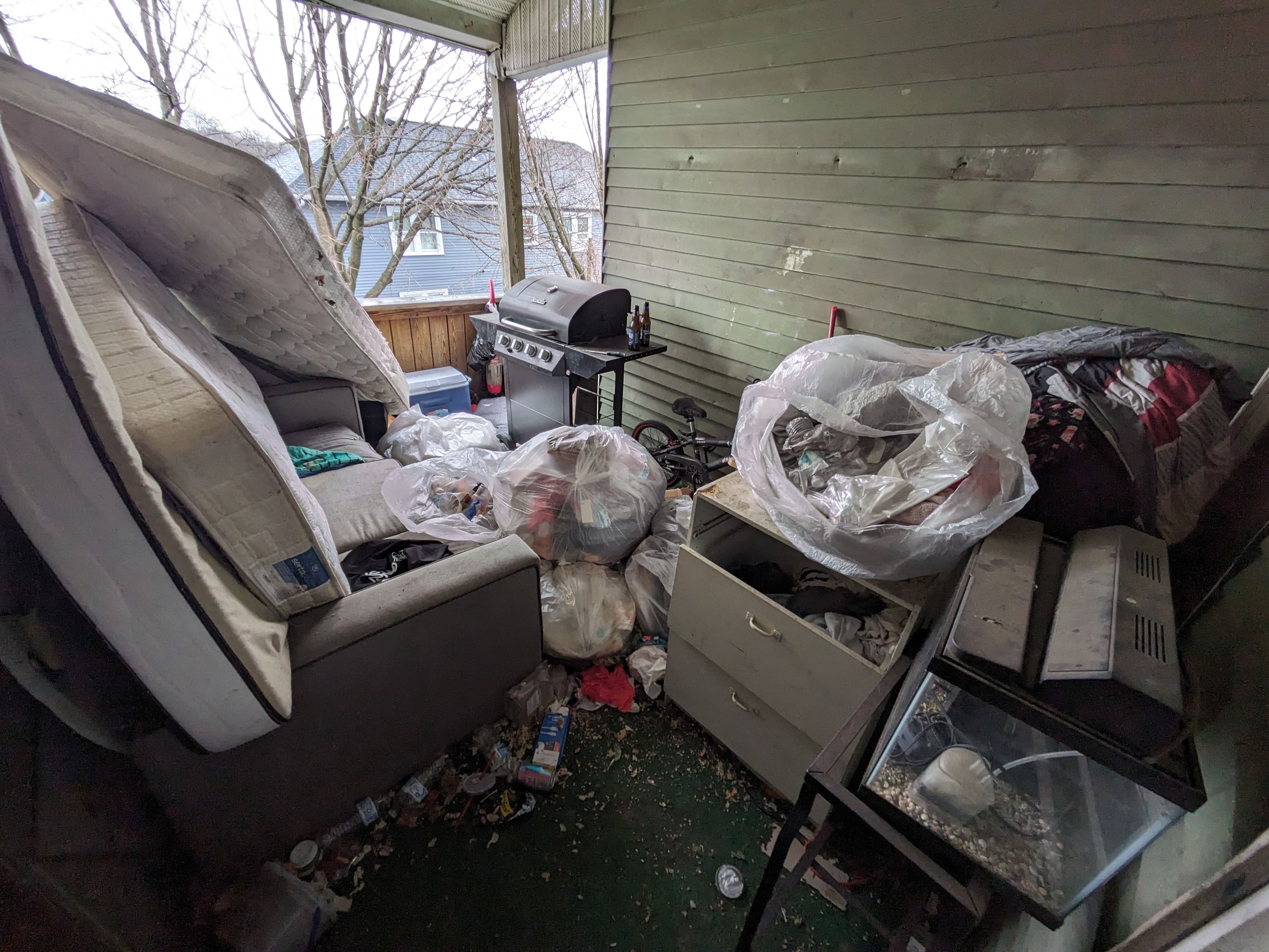 Cluttered porch filled with trash, furniture, and discarded items in disarray.