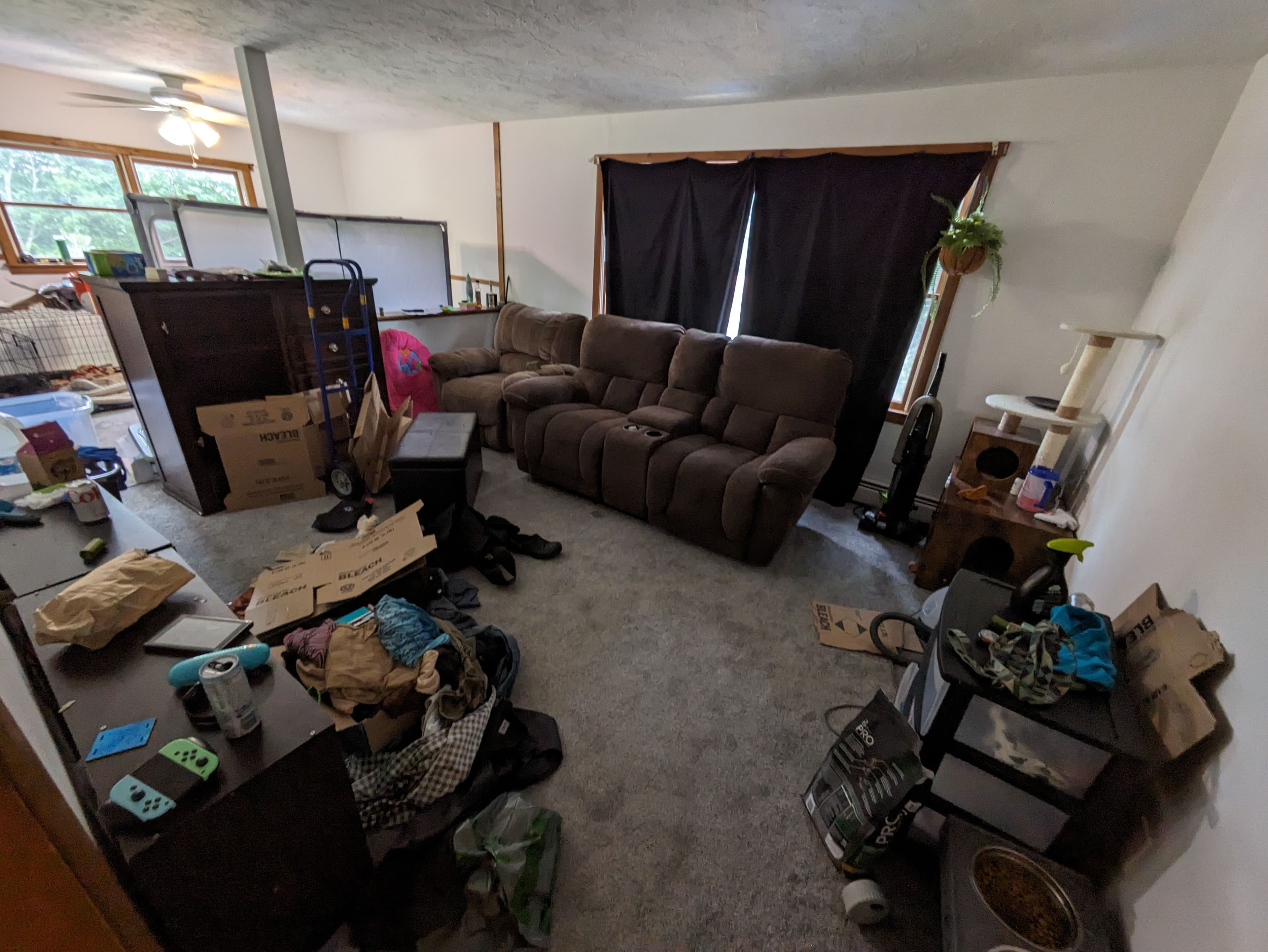 Cluttered living room with a brown couch, cardboard boxes, and scattered belongings.