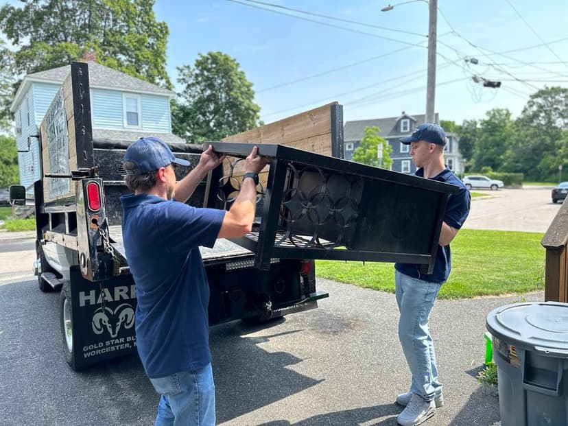 Two movers lifting a large black table from a truck on a residential street.