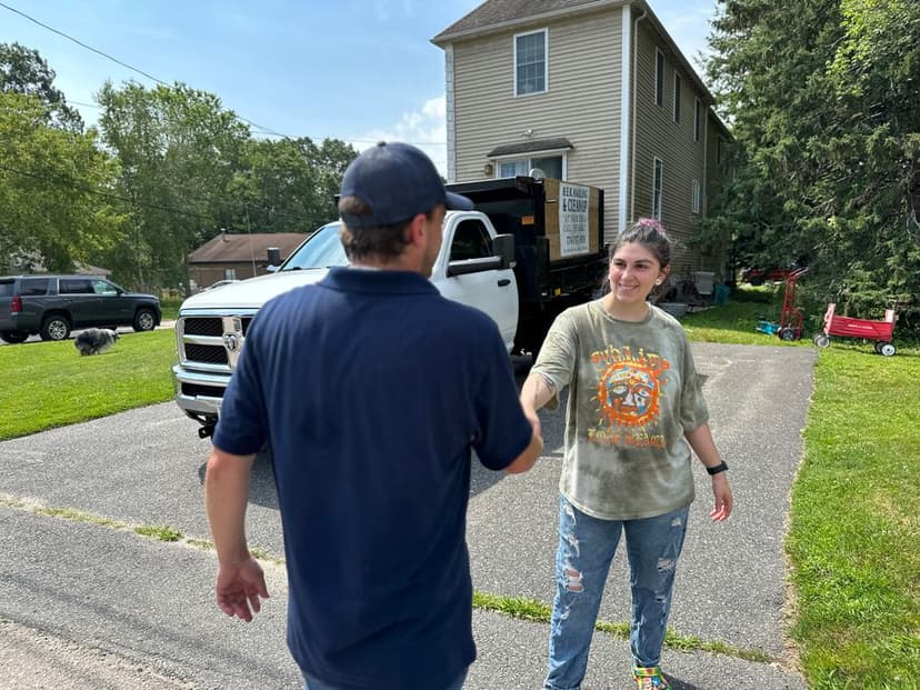 Person shaking hands with a contractor in front of a house and truck on a sunny day.